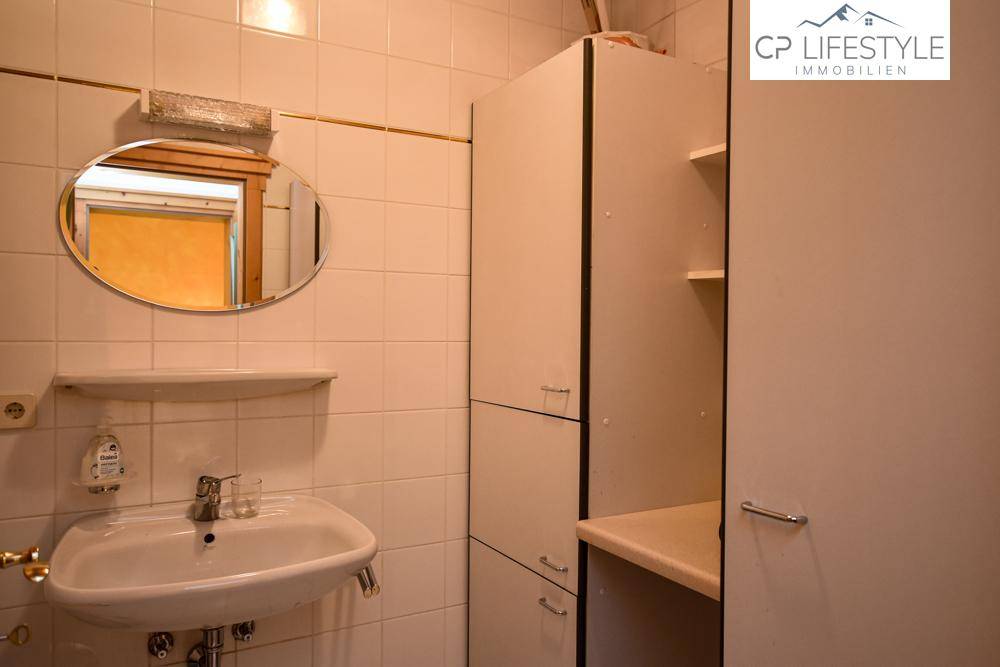 Funktionales Badezimmer mit Waschbecken, Spiegel, weißen Fliesen und praktischen Stauschränken.