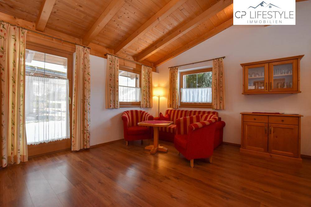 Helles Wohnzimmer mit Holzbalkendecke, traditionellen Möbeln und Zugang zu einem Außenbereich, umgeben von Natur.