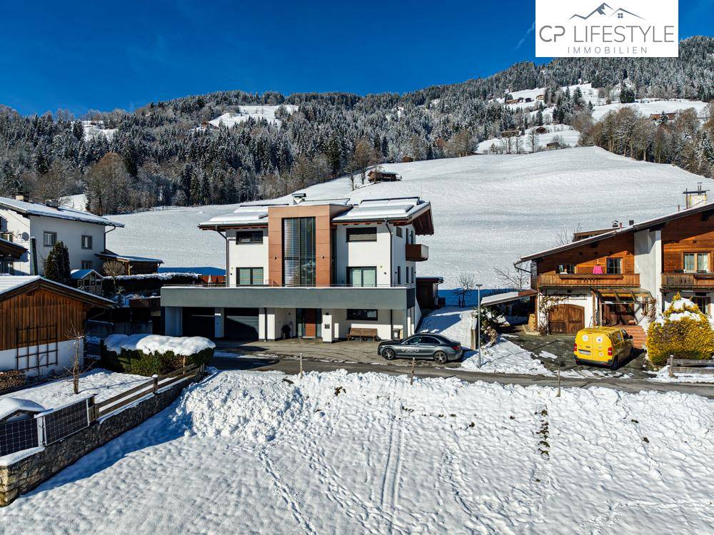 Modernes Wohnhaus mit Garage und Zufahrt, eingebettet in eine verschneite Berglandschaft.