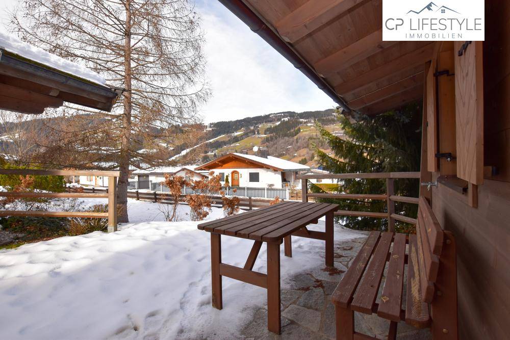 Rustikale Terrasse mit Holztisch und Bänken, umgeben von Schnee und mit Blick auf die umliegende Berglandschaft.