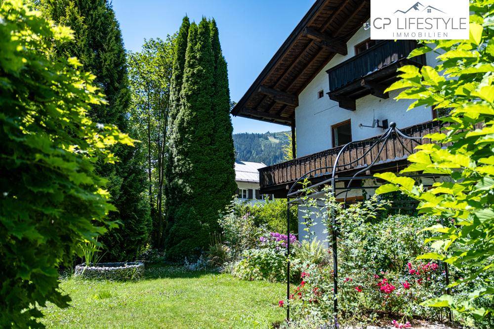 Gepflegter Gartenbereich mit Rasen, Blumenbeeten und hohen Bäumen neben dem Haus.