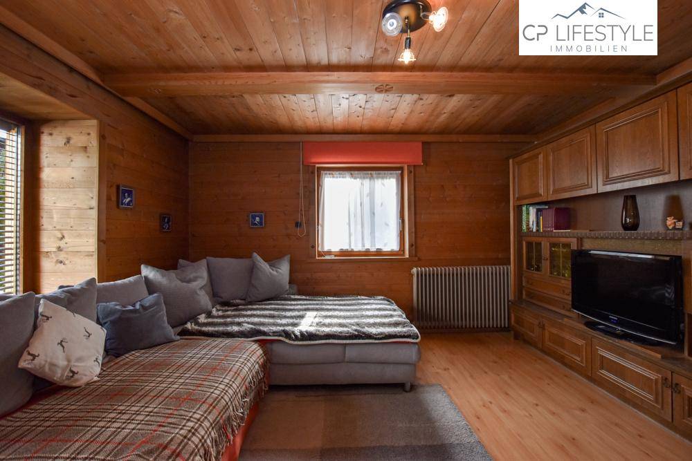 Rustikales Wohnzimmer mit Holzwänden, Holzbalkendecke und gemütlicher Sitzecke.