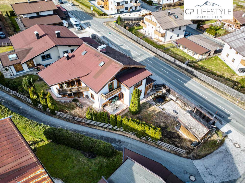 Luftaufnahme des Hauses mit rotem Satteldach, umgeben von einer gepflegten Hecke und Straße.