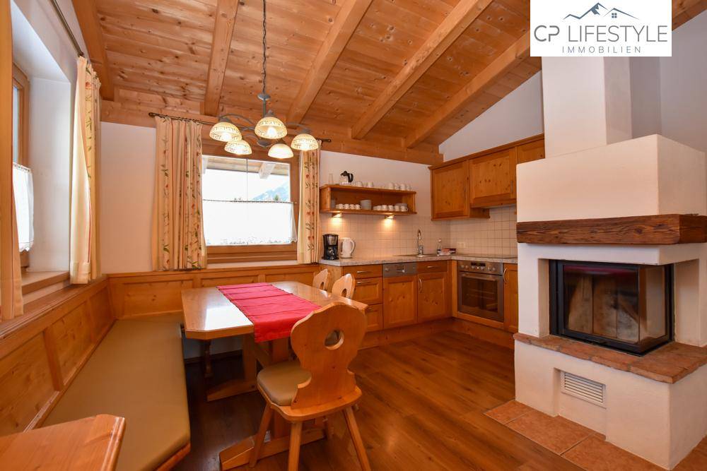 Gemütliche Holzküche im Landhausstil mit Essbereich, Kamin und Blick auf die verschneite Landschaft.