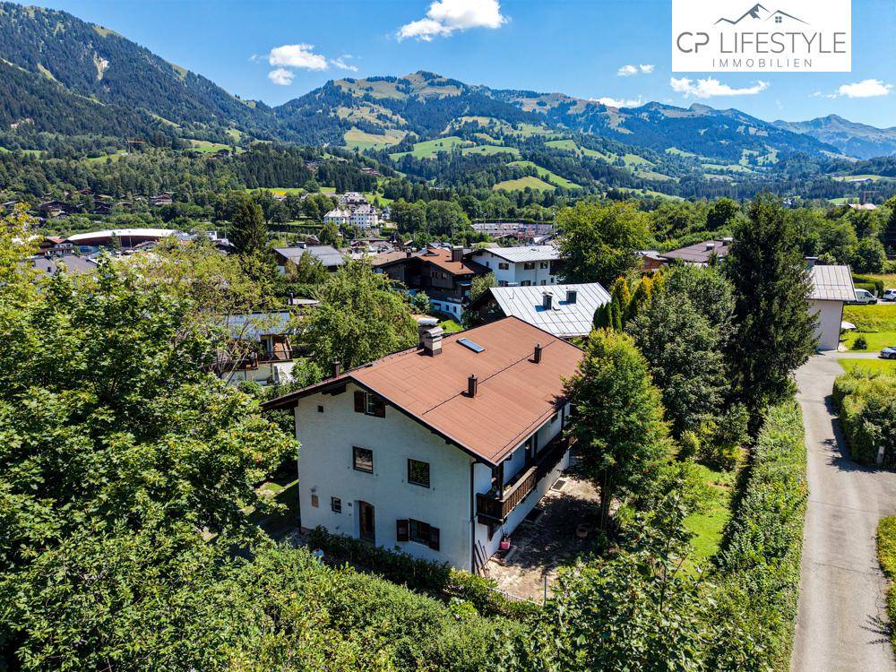 Panoramablick auf ein Wohnhaus mit braunem Dach, umgeben von üppiger grüner Landschaft und Bergen.