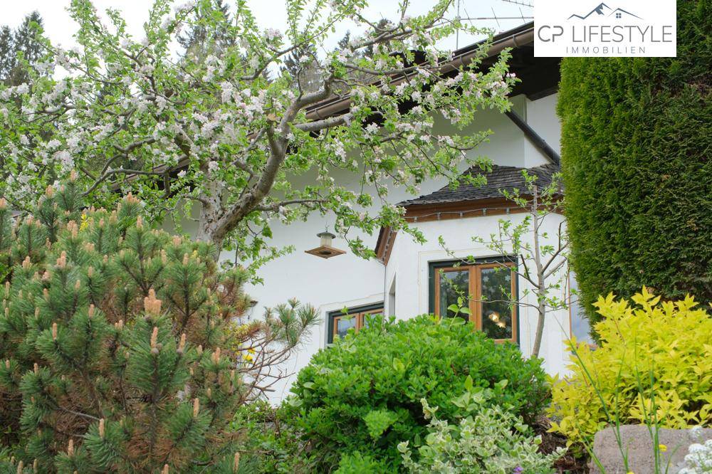 Detailansicht des Hauses mit blühendem Apfelbaum und gepflegter Bepflanzung.