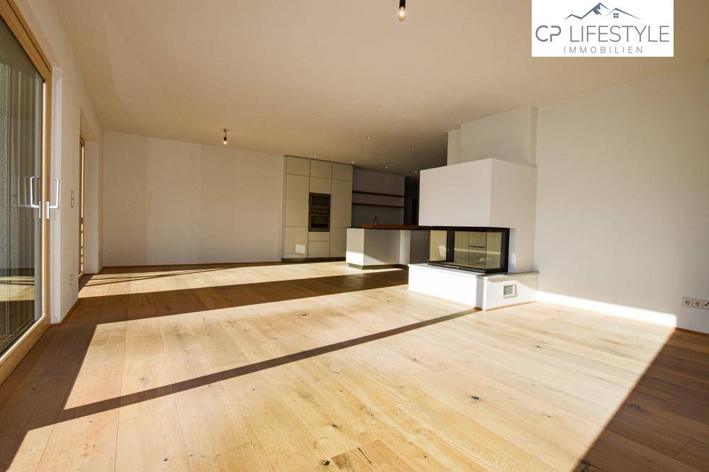 Geräumiger offener Wohnbereich mit Kamin und Blick auf die moderne Küche im Hintergrund.