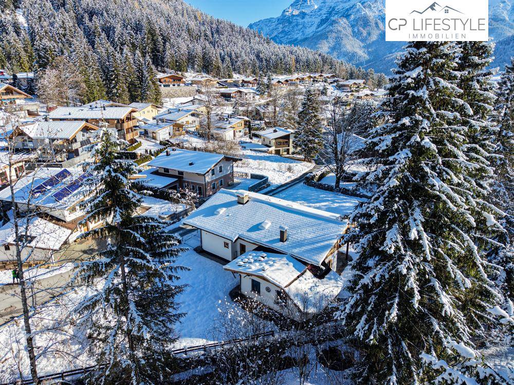 Verschneites Dorf in den Bergen, umgeben von dichten Wäldern und einer malerischen Winterlandschaft.