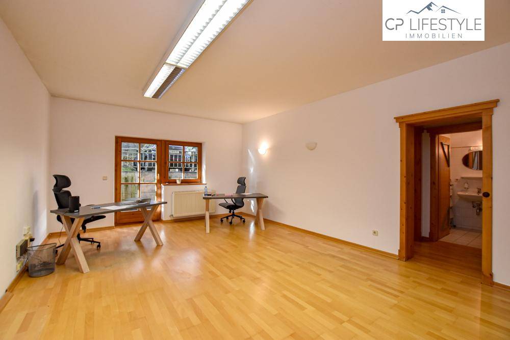 Geräumiges Büro mit hellem Holzfußboden, zwei Schreibtischen und natürlichem Lichteinfall durch die Fenstertüren.