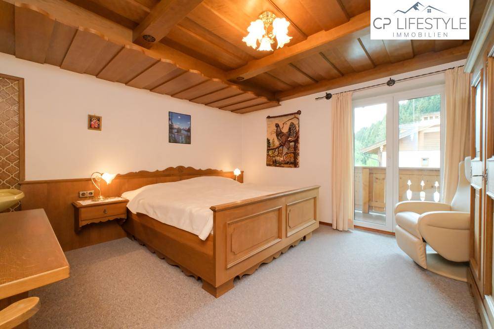 Helles Schlafzimmer mit traditionellem Holzbett, Holzdecke und Balkonzugang.