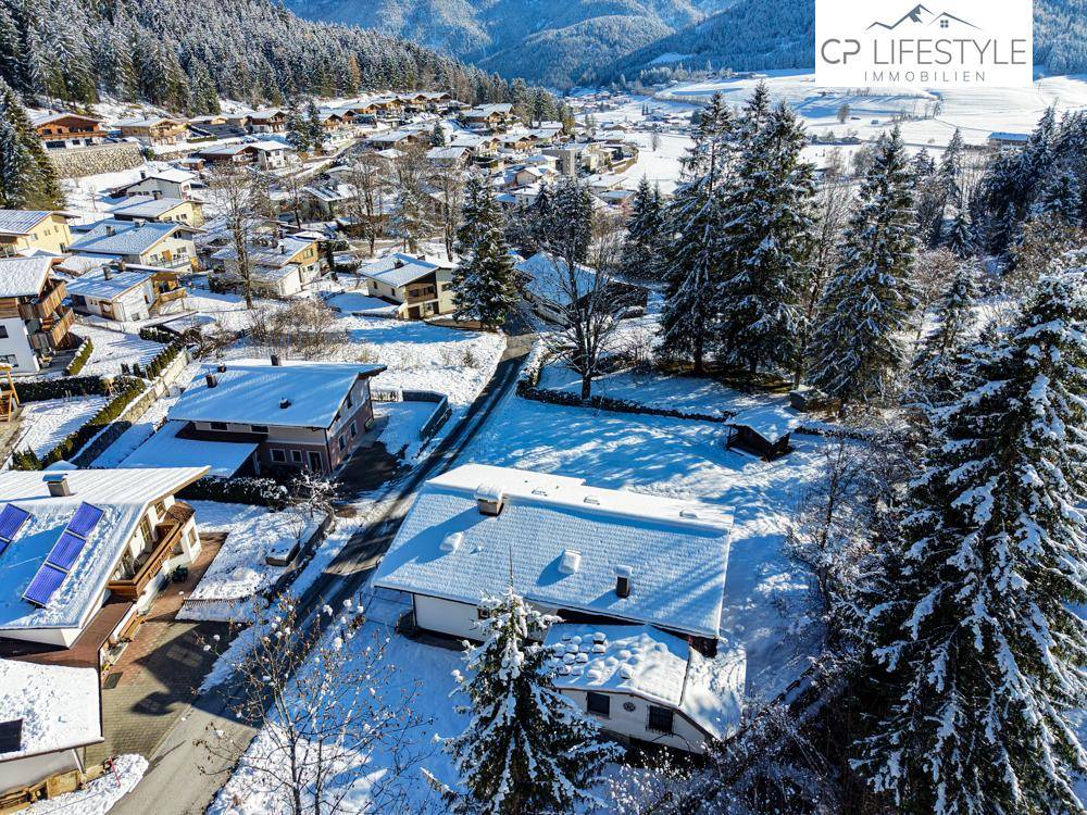 Verschneite Siedlung in einem Tal, umgeben von bewaldeten Bergen und einer winterlichen Atmosphäre.