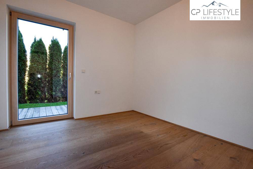 Helles Zimmer mit Holzboden und großem Fenster, das den Blick ins Grüne freigibt.
