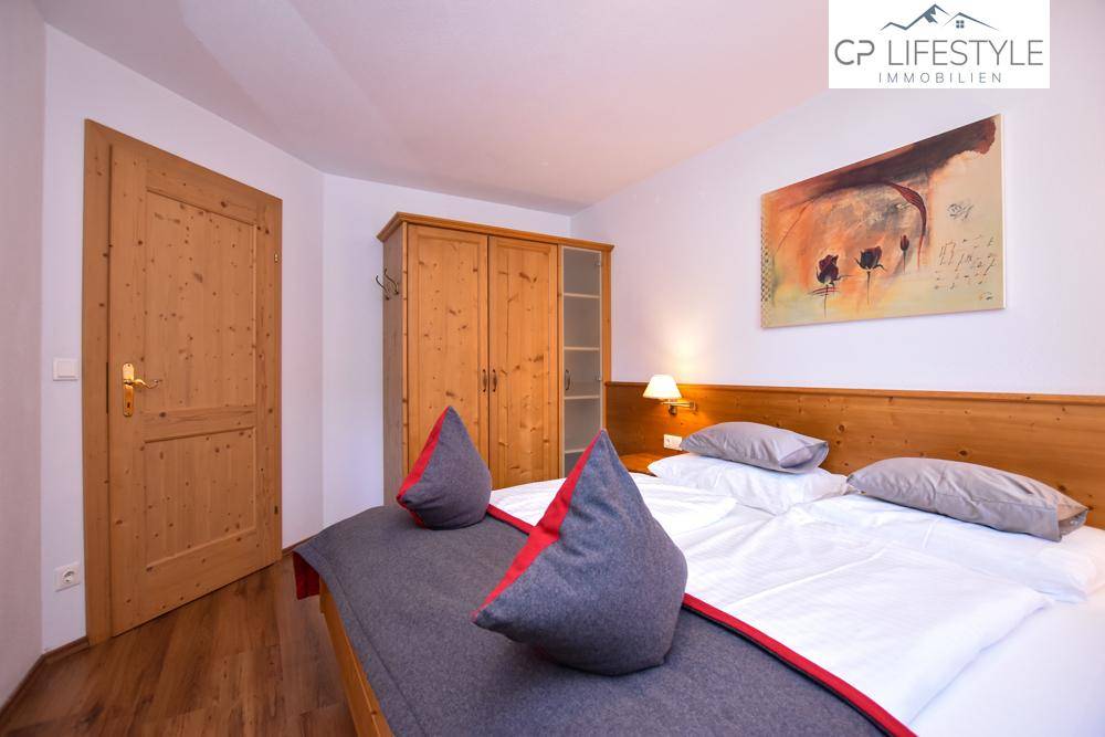 Komfortables Schlafzimmer mit Holzbett, Kleiderschrank und einem Fenster, das viel Tageslicht hereinlässt.