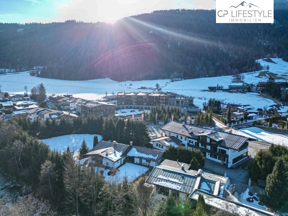 Luftaufnahme einer Siedlung in den Bergen mit Sonnenstrahlen und verschneiter Landschaft.