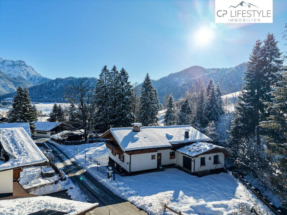 Charmantes Haus mit schneebedecktem Dach und Vorgarten, eingebettet in eine winterliche Berglandschaft.