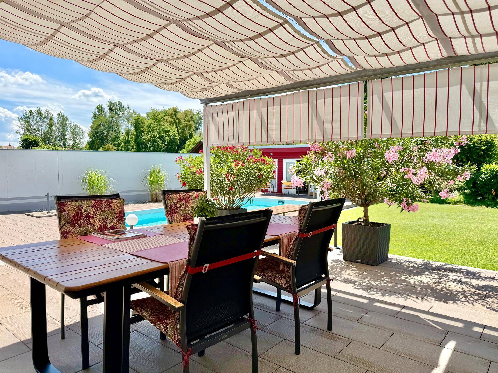 Überdachte Terrasse mit Esstisch und Blick auf den Pool und den grünen Gartenbereich.
