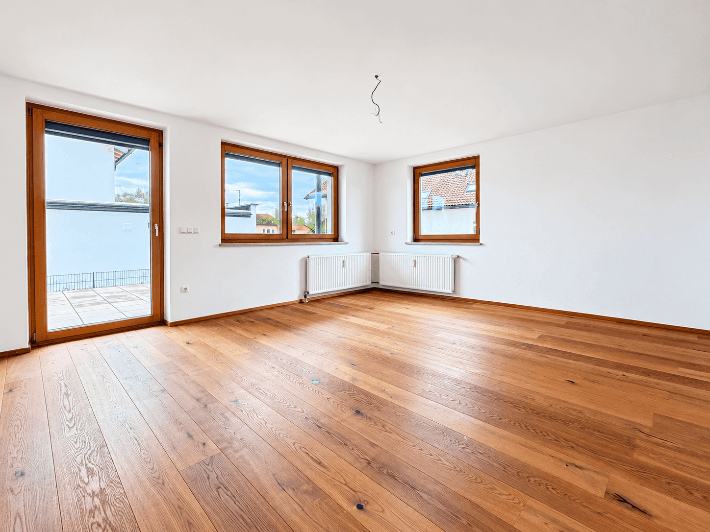 Geräumiges, helles Zimmer mit Holzboden und mehreren Fenstern sowie Terrassenzugang.