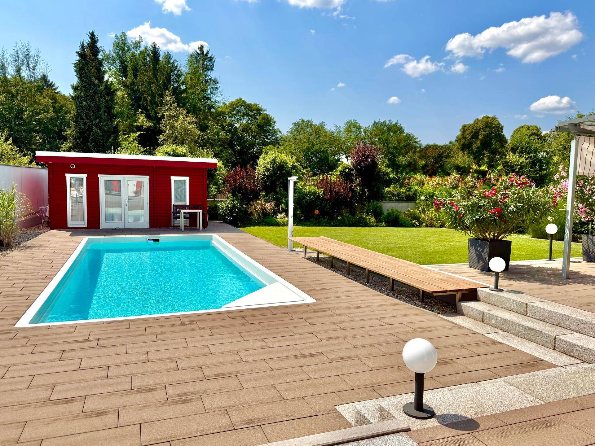 Weitläufiger Gartenbereich mit Pool, Liegefläche und einem roten Gartenhaus unter strahlendem Sonnenschein.