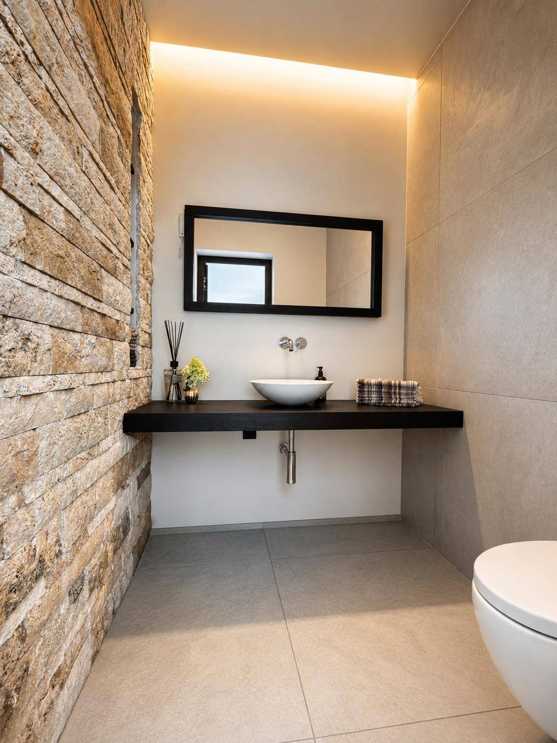 Stilvolles Gäste-WC mit Natursteinwand, modernem Waschbecken und indirekter Beleuchtung.