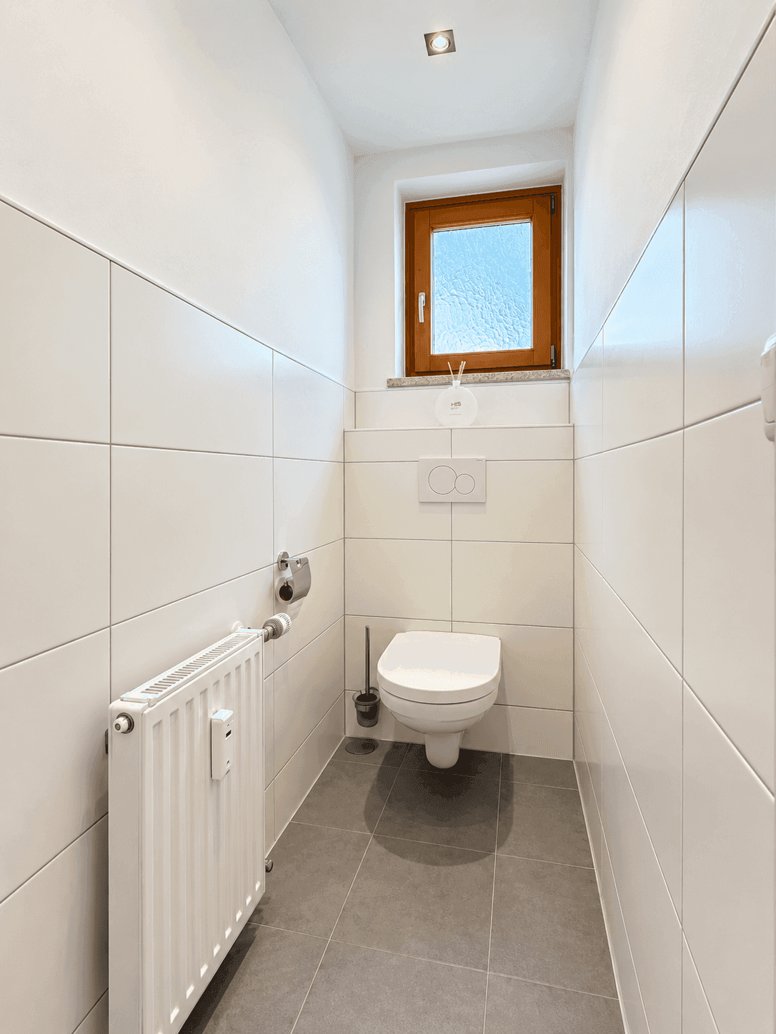 Kleines Gäste-WC mit wandhängender Toilette, Fenster und Fliesenboden.