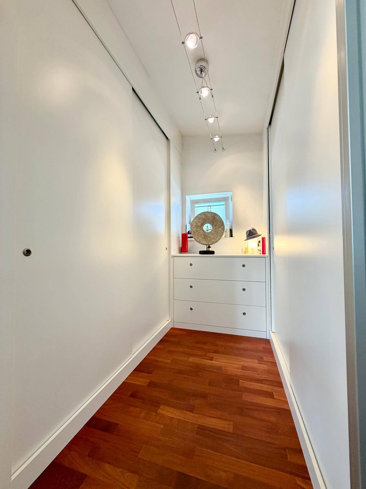 Praktischer begehbarer Kleiderschrank mit Holzboden und integrierter Kommode für viel Stauraum.