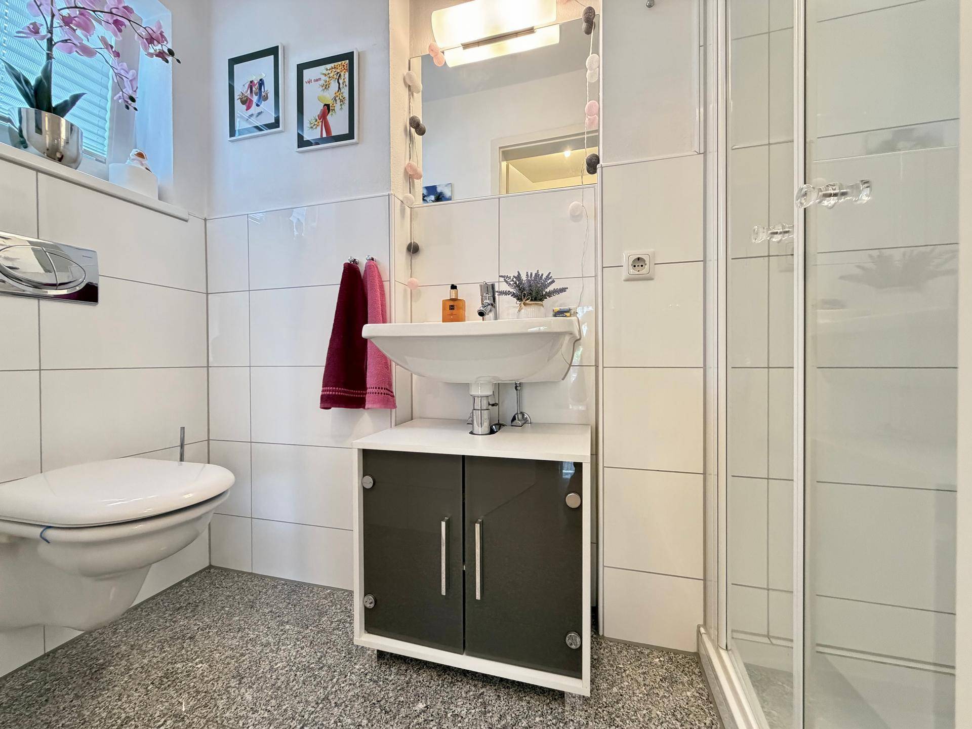 Modernes Badezimmer mit Fliesenboden, Waschbecken, Toilette und Duschkabine, hell und funktional.