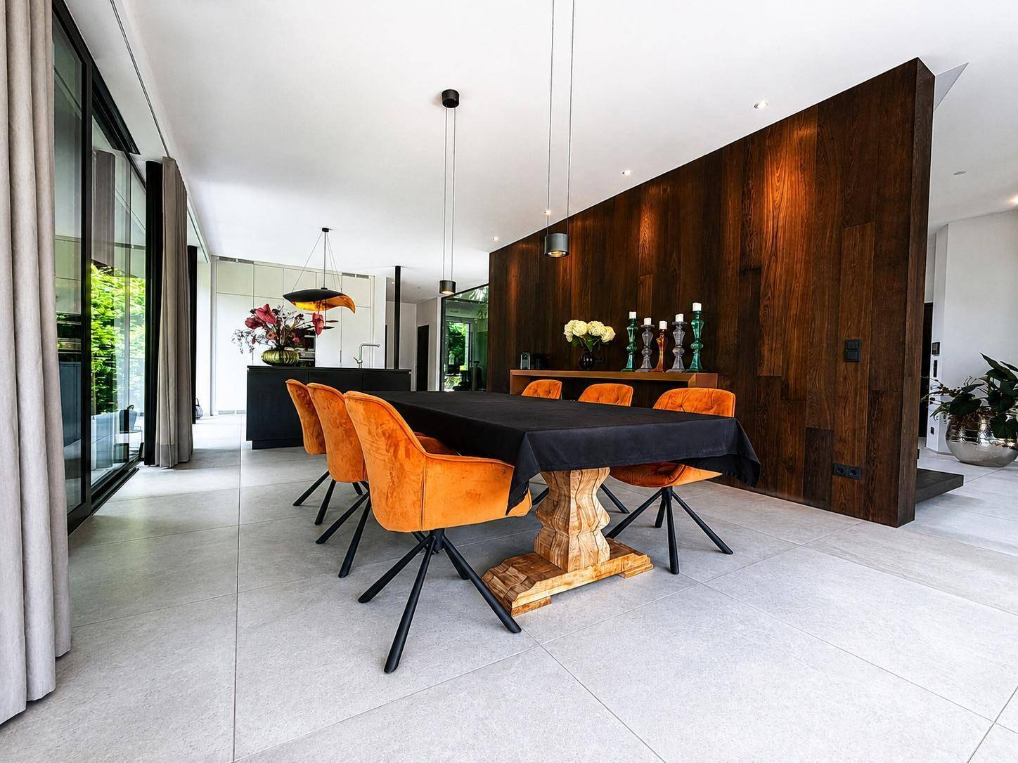 Eleganter Essbereich mit großem Holztisch, orangefarbenen Stühlen und Holzwand in offenem Konzept.