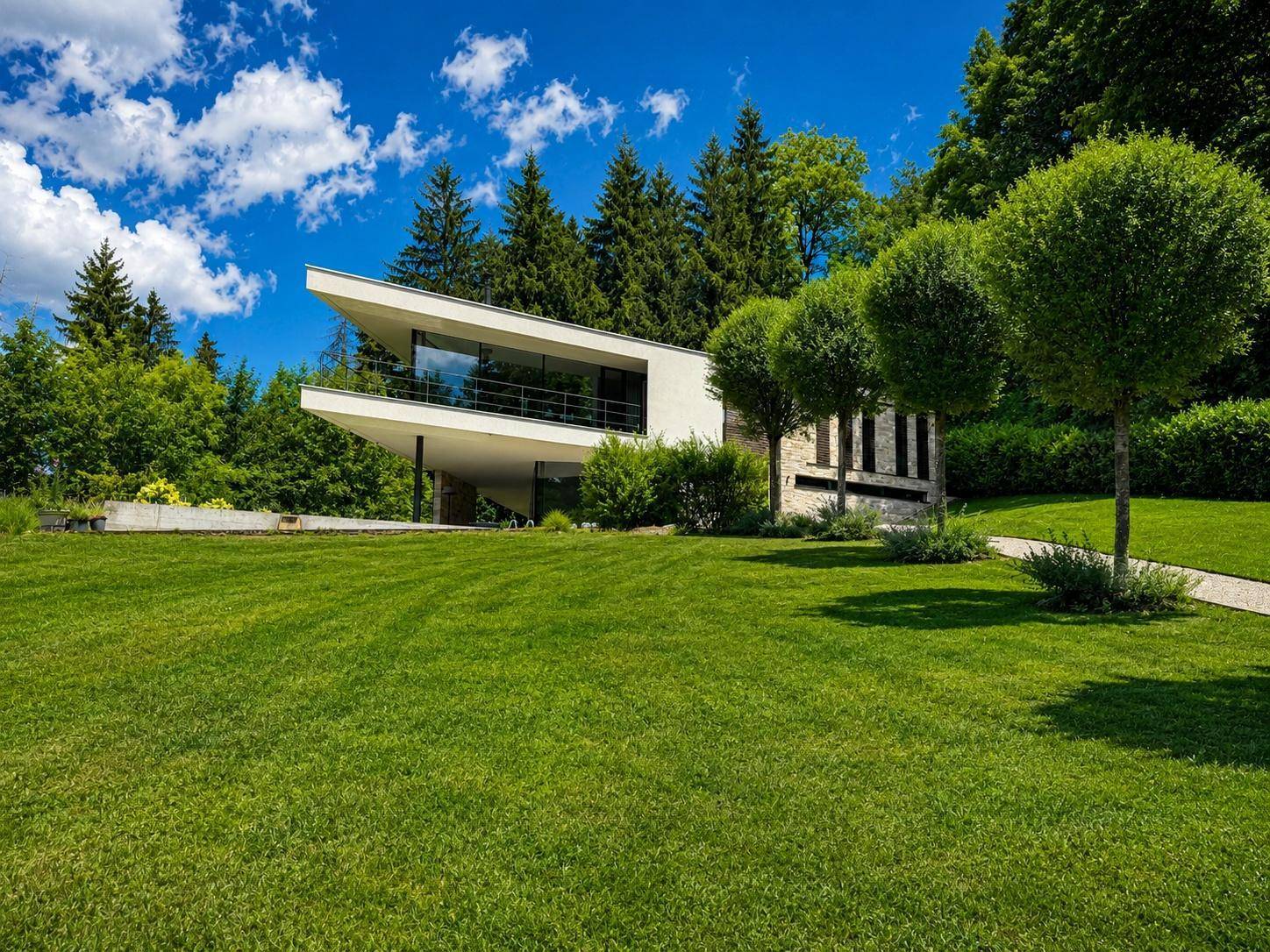 Moderne Architektur der Villa eingebettet in eine weitläufige grüne Landschaft mit Bäumen und Rasen.