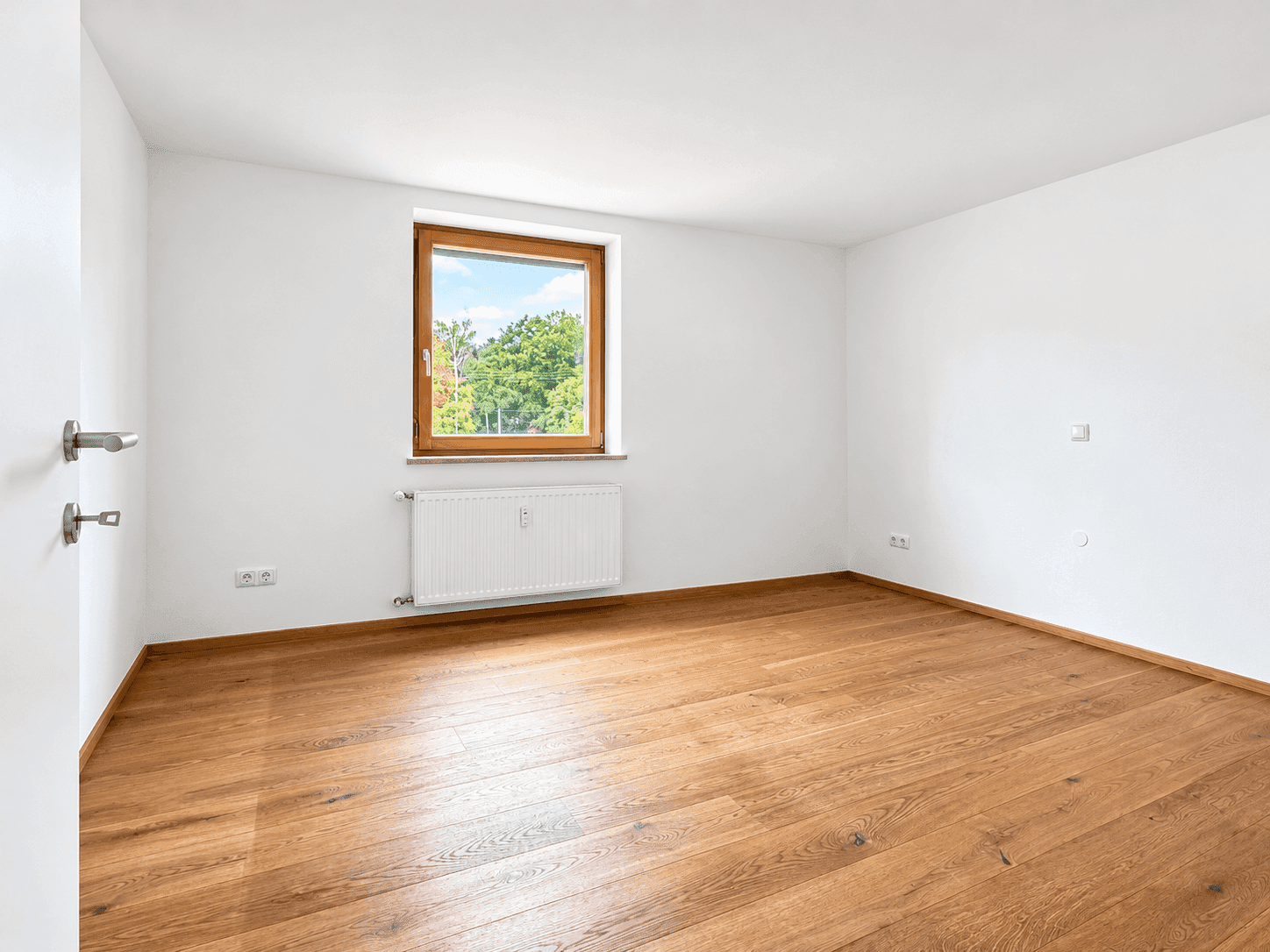 Helles Schlafzimmer mit Holzboden und Fenster mit Blick ins Grüne.