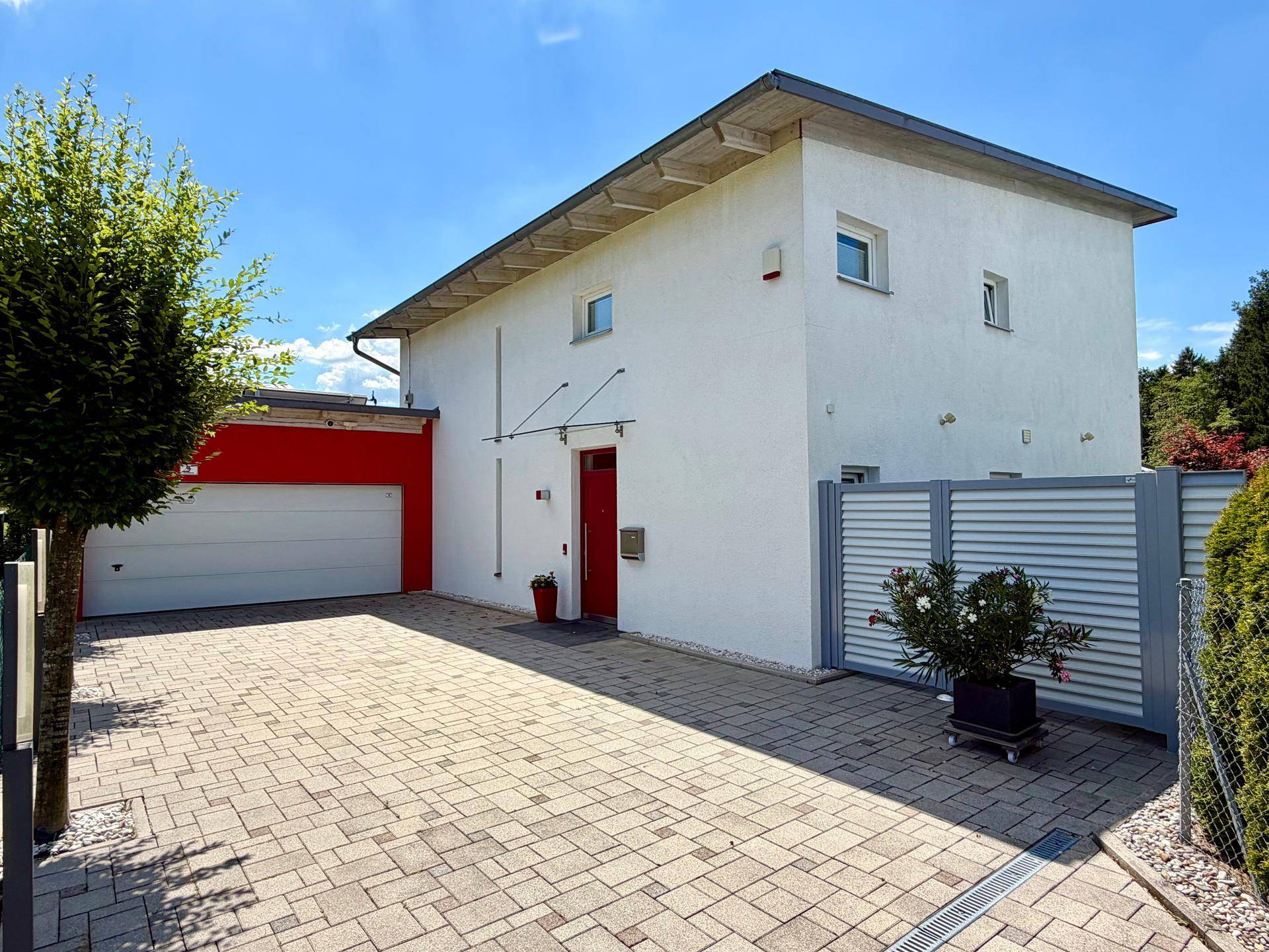 Moderne Hausfassade mit Garagenzufahrt und gepflastertem Vorplatz unter blauem Himmel.