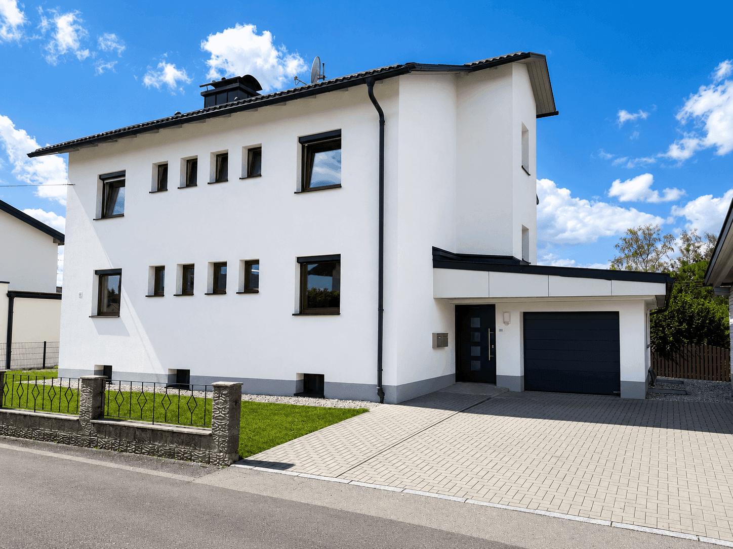 Modernes weißes Einfamilienhaus mit integrierter Garage und gepflasterter Auffahrt.