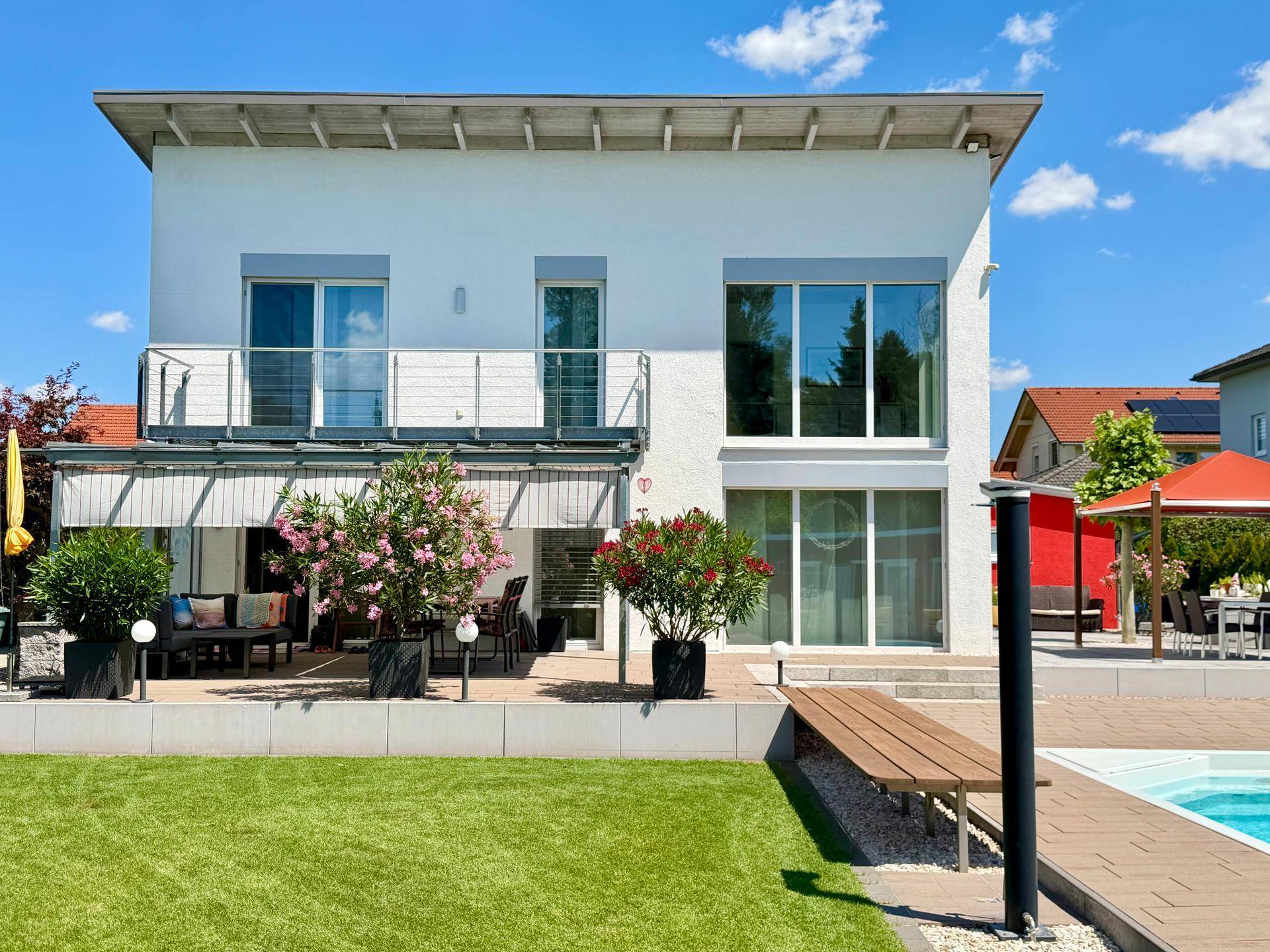 Modernes Wohnhaus mit Garten, Pool und großer Terrasse unter blauem Himmel.