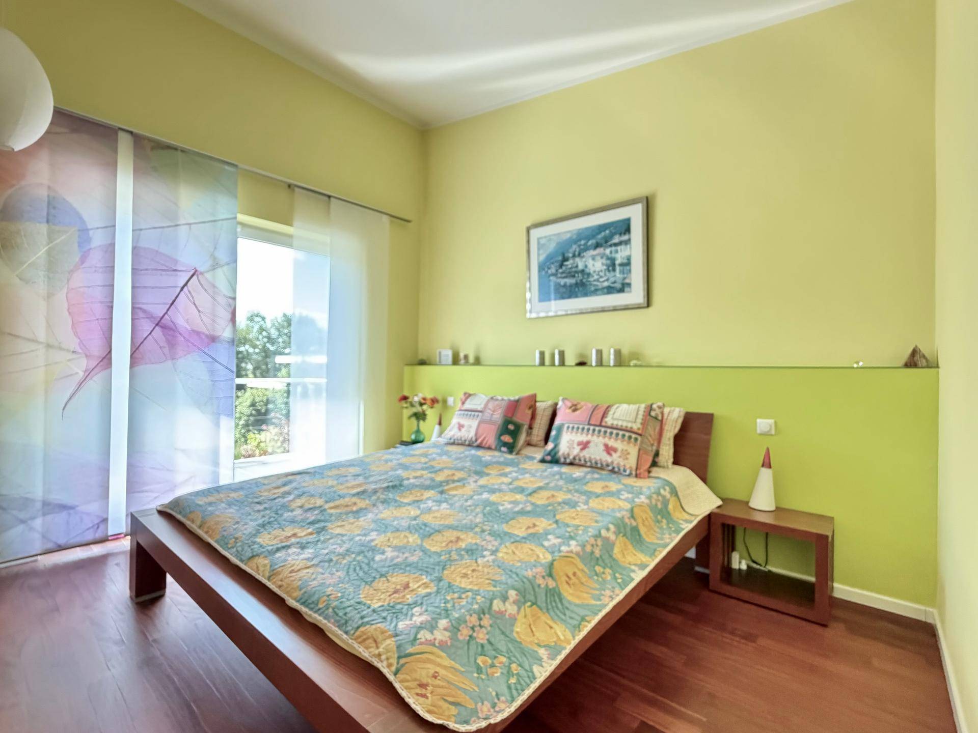 Helles Schlafzimmer mit Holzboden, grünen Wänden und direktem Zugang zum Balkon.