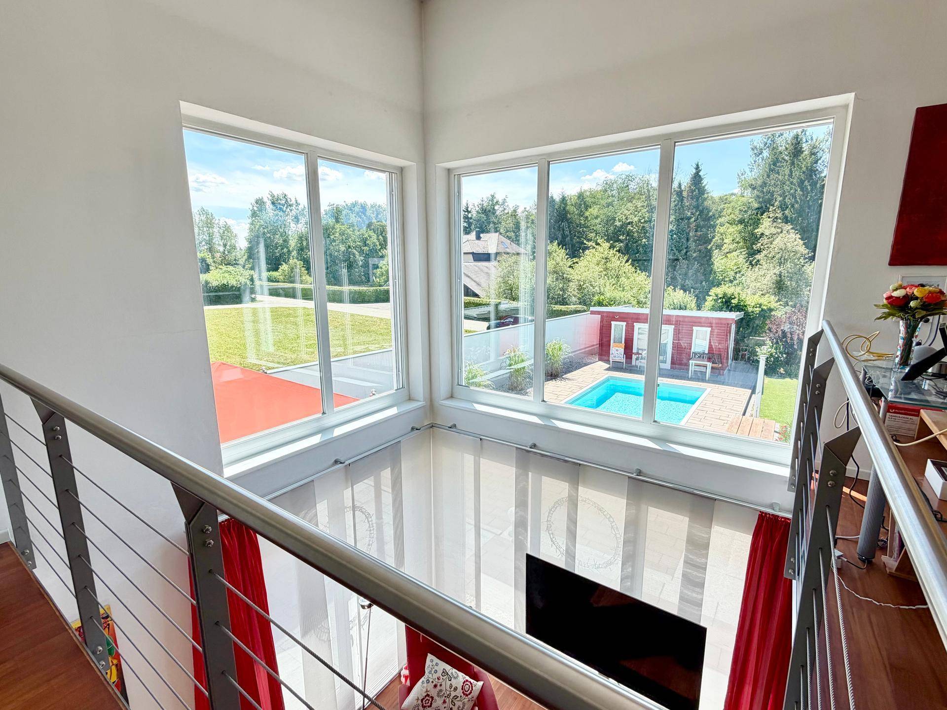 Offener Wohnbereich mit großen Fenstern und weitem Blick auf den Garten und den Pool.