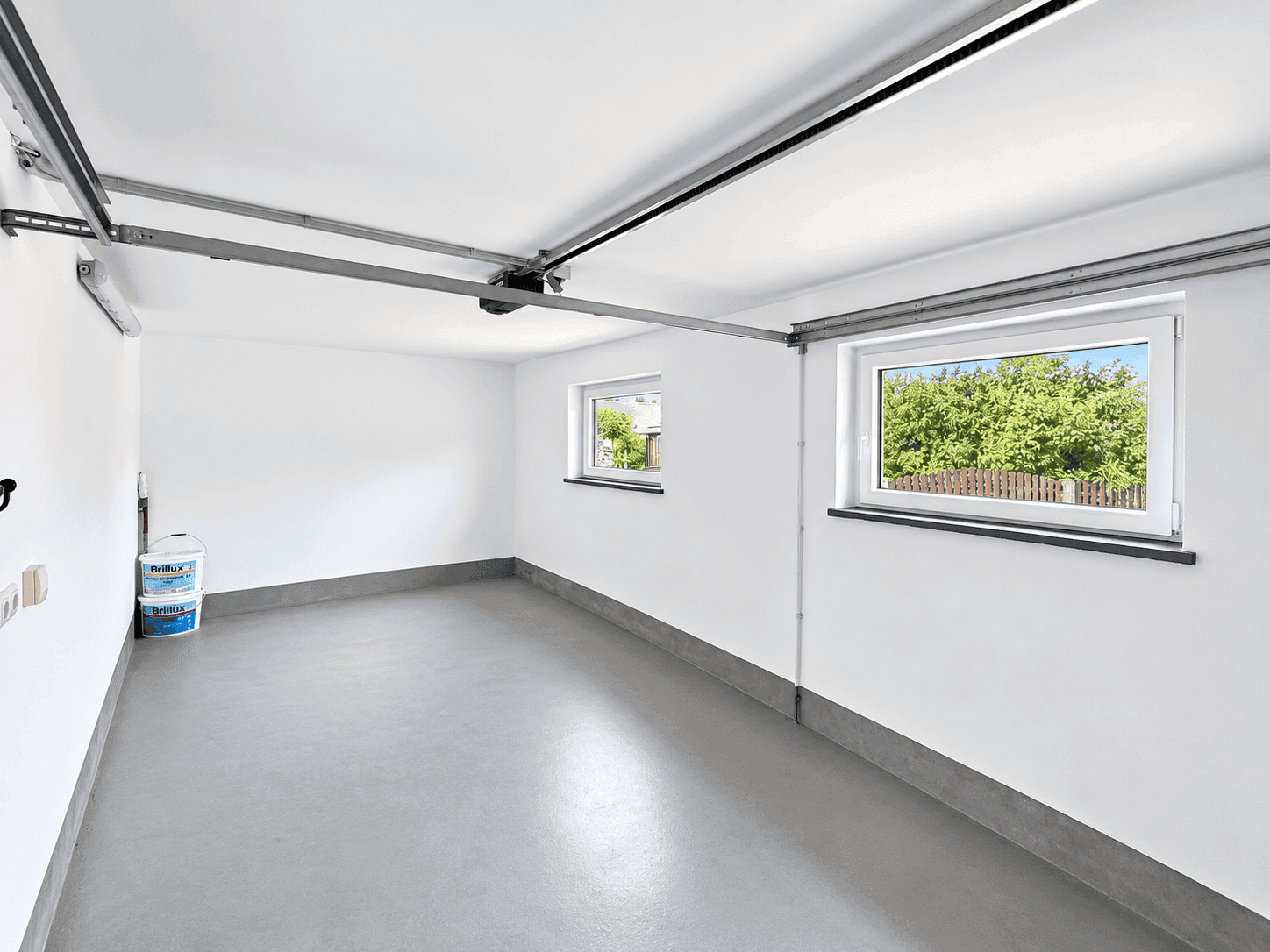 Saubere und helle Garage mit zwei Fenstern und grauem Boden.