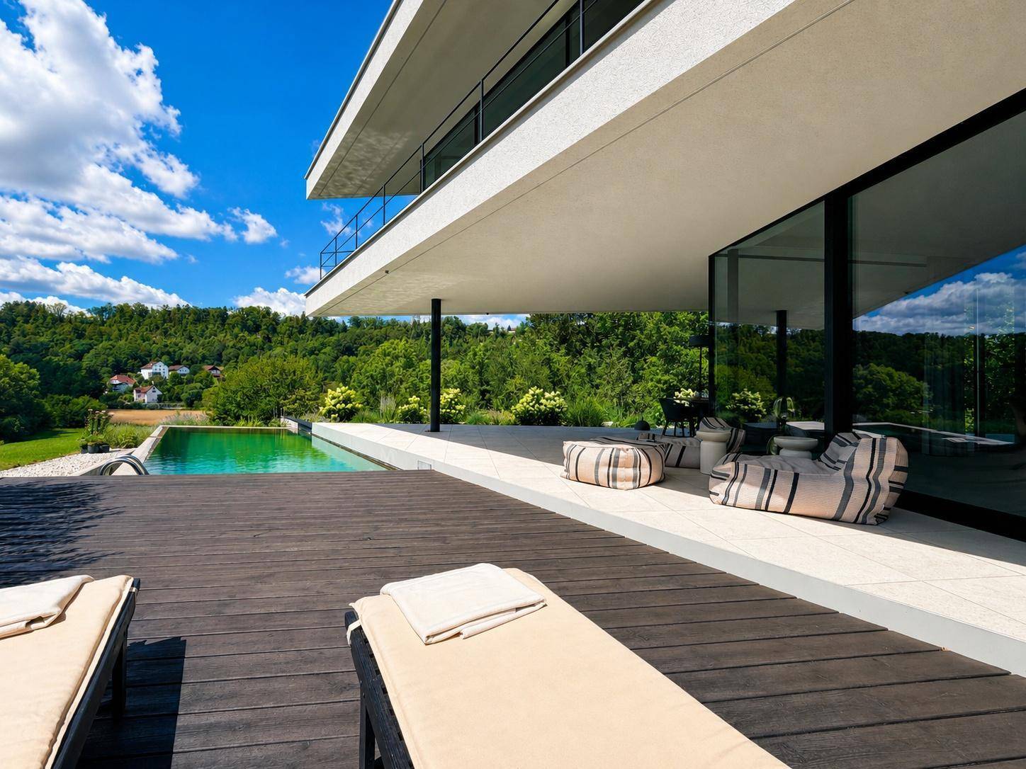 Entspannungsbereich auf der Holzterrasse mit Liegestühlen und Blick auf den Pool und die grüne Landschaft.