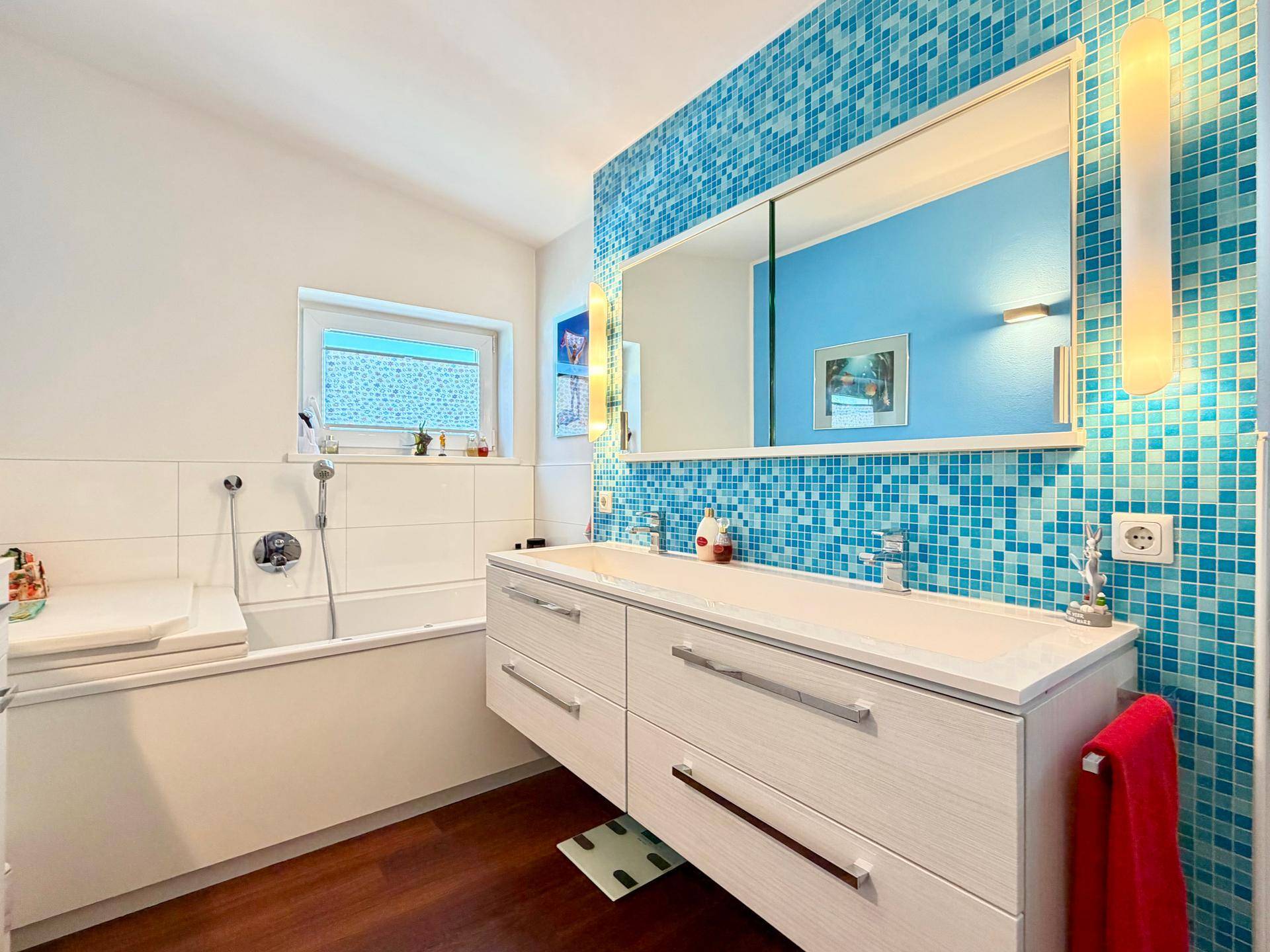 Modernes Badezimmer mit blauen Mosaikfliesen, Doppelwaschbecken und integrierter Badewanne.