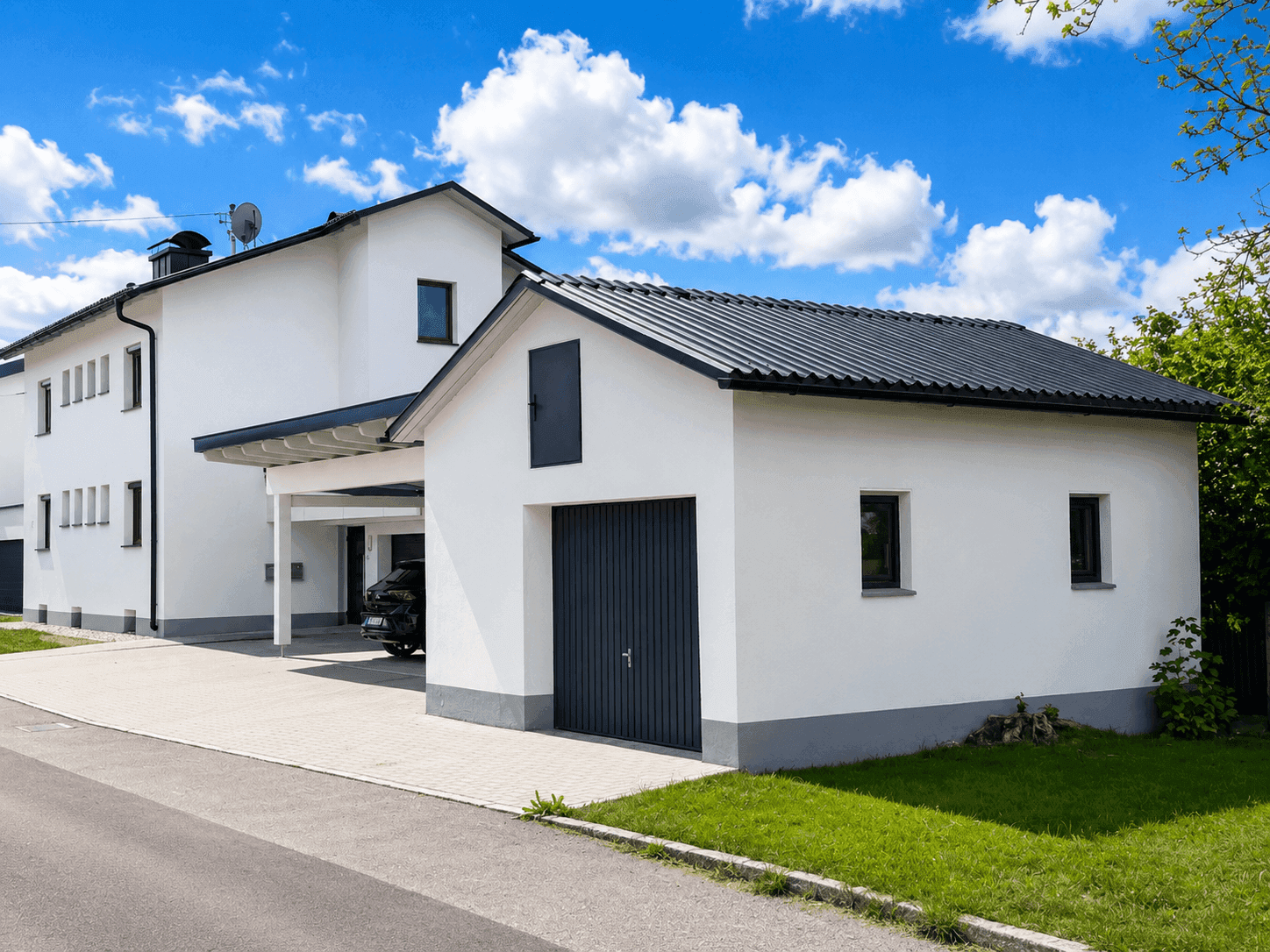 Weißes Einfamilienhaus mit separater Garage und Carport auf gepflegtem Grundstück.