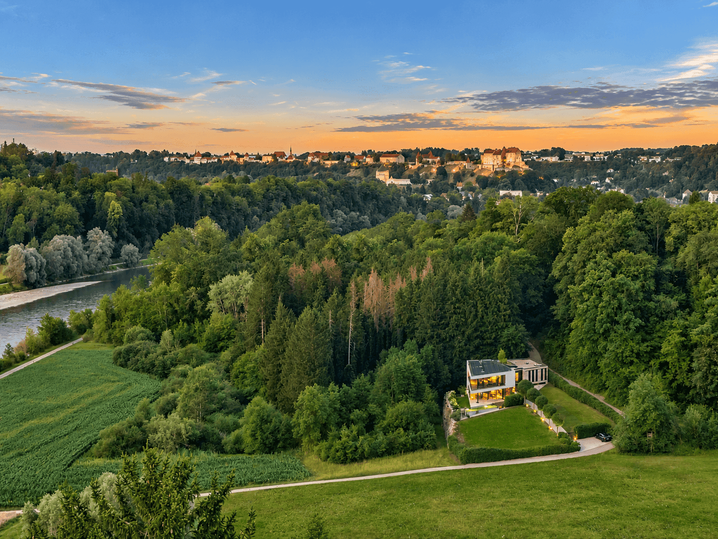 Panoramablick auf die moderne Villa eingebettet in eine grüne Landschaft mit Fluss und ferner Stadtansicht.