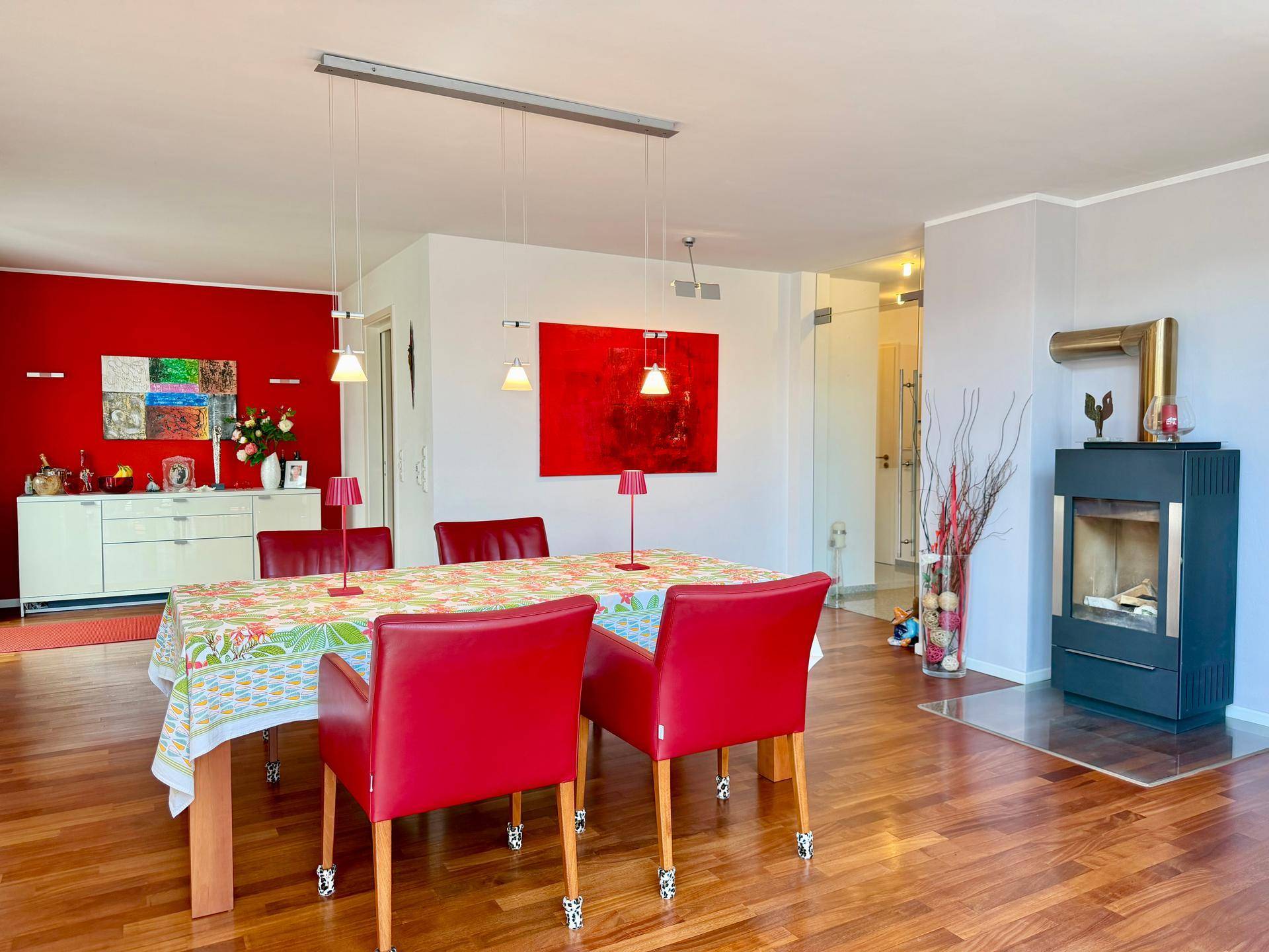 Geräumiger Essbereich mit Holzboden, roter Akzentwand und modernem Kaminofen für Gemütlichkeit.