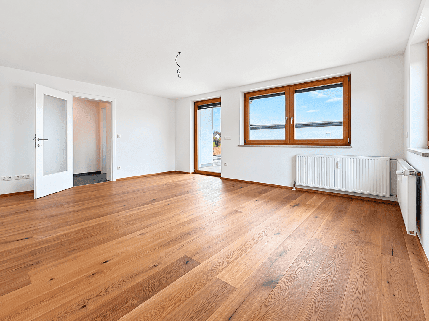 Helles, leeres Zimmer mit Holzboden und Zugang zu einem möglichen Außenbereich.