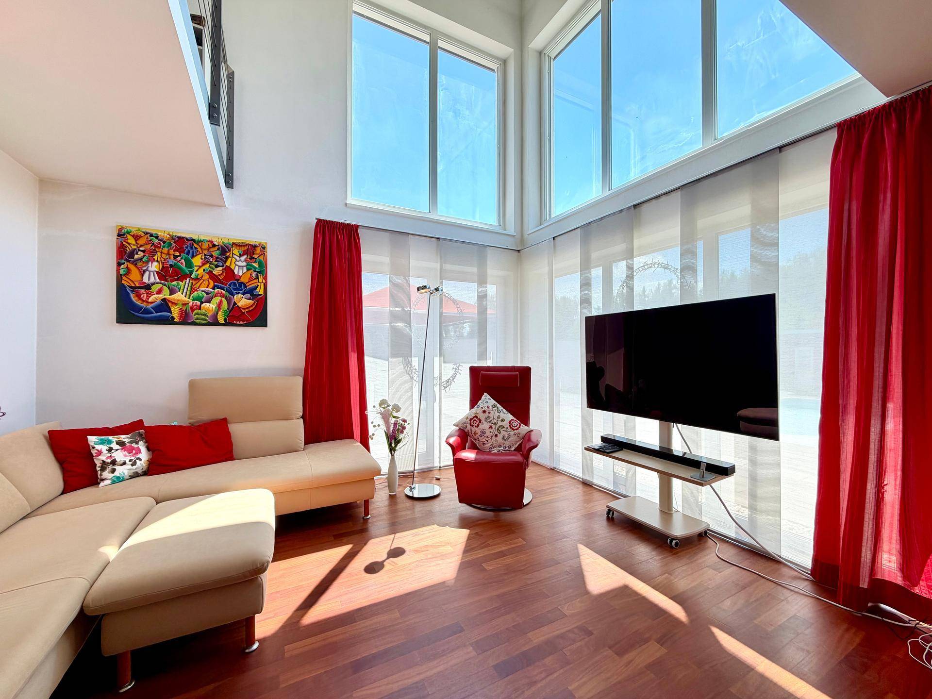 Helles Wohnzimmer mit hohen Decken, großen Fenstern und Holzboden, lichtdurchflutet und modern.