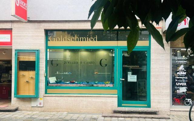 Nahaufnahme einer Goldschmied-Ladenfront mit großen Schaufenstern und einem markanten grünen Rahmen.