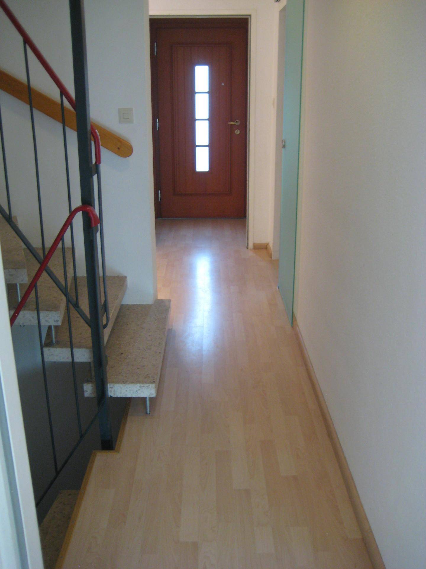 Heller Flur mit Laminatboden, einer Treppe und einer Holztür am Ende des Ganges.