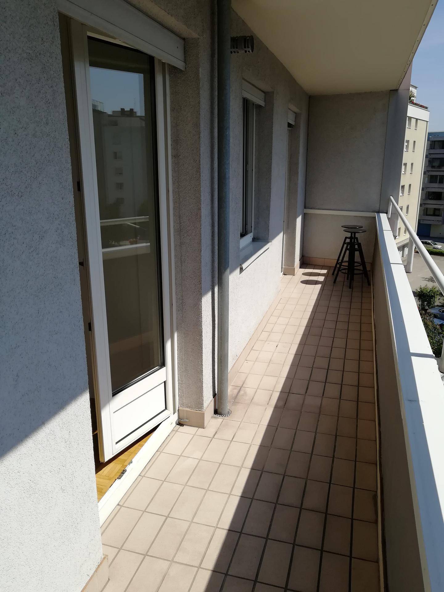 Langer, schmaler Balkon mit Fliesenboden und Blick auf die umliegenden Gebäude.