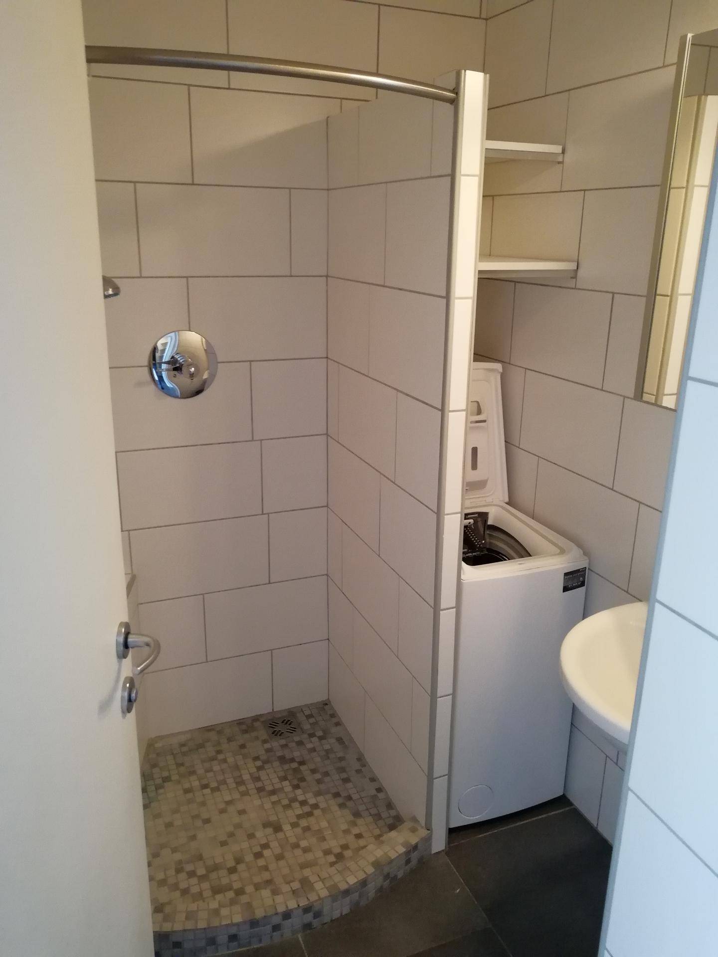 Modernes Badezimmer mit Duschkabine, Waschbecken und integrierter Waschmaschine.