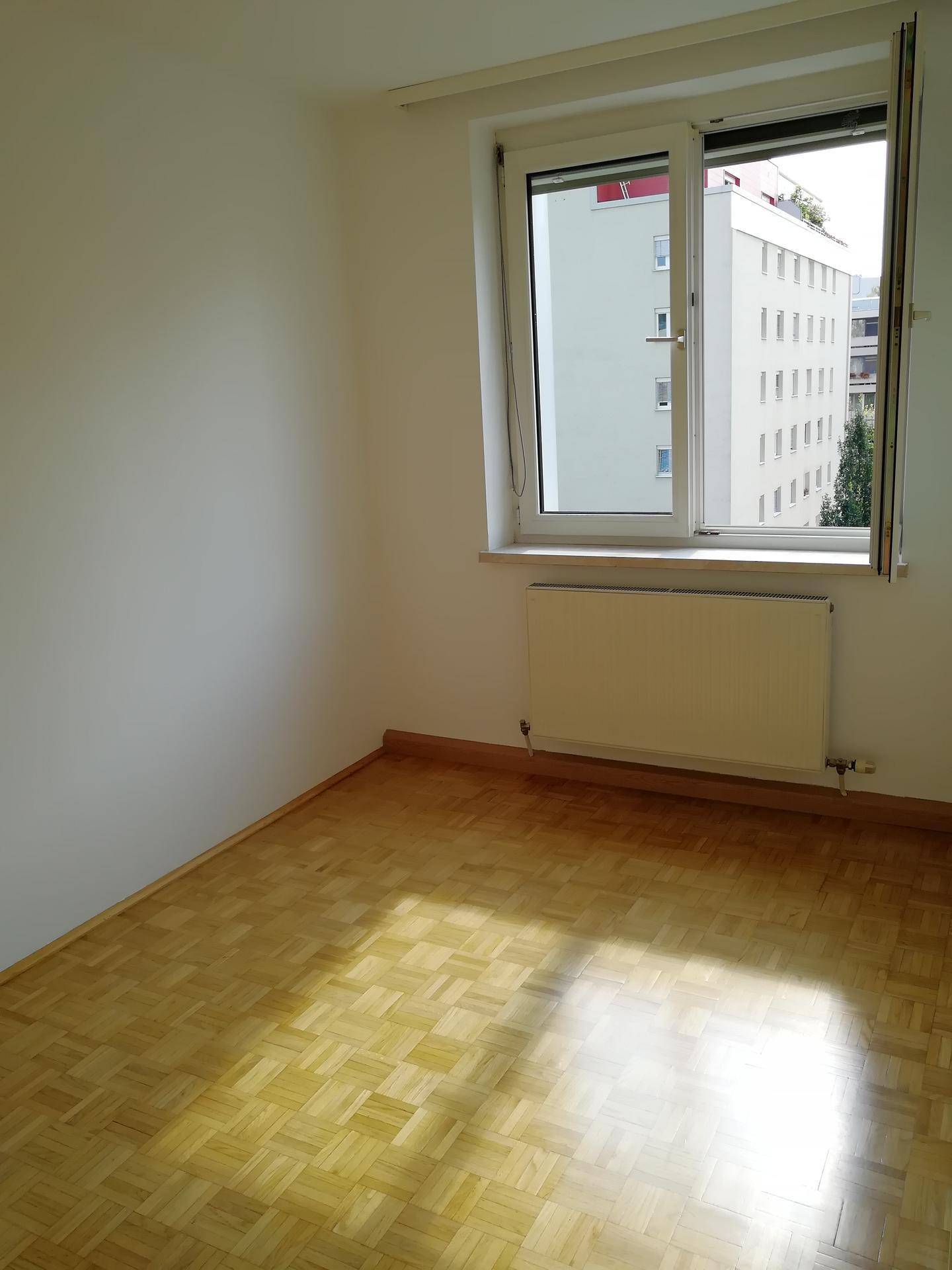 Helles Zimmer mit Parkettboden und großem Fenster, ideal als Schlaf- oder Arbeitszimmer.
