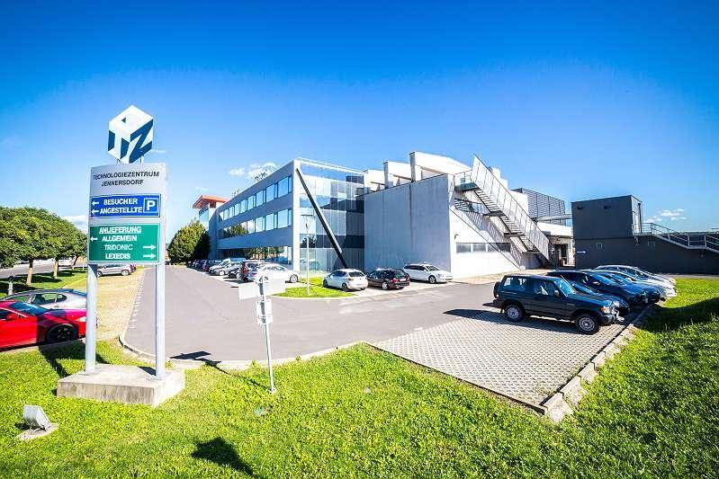 Ansicht des modernen Bürogebäudes mit Parkplätzen und grüner Umgebung unter blauem Himmel.