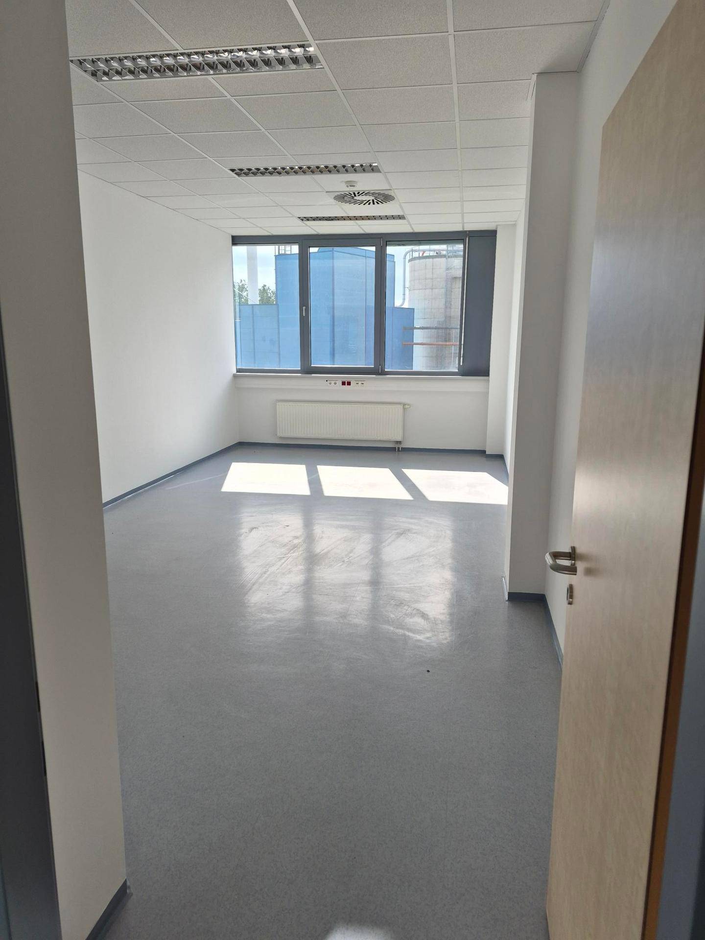 Kleinerer, heller Büroraum mit großen Fenstern, grauem Boden und weißen Wänden, ideal für Einzelbüros.