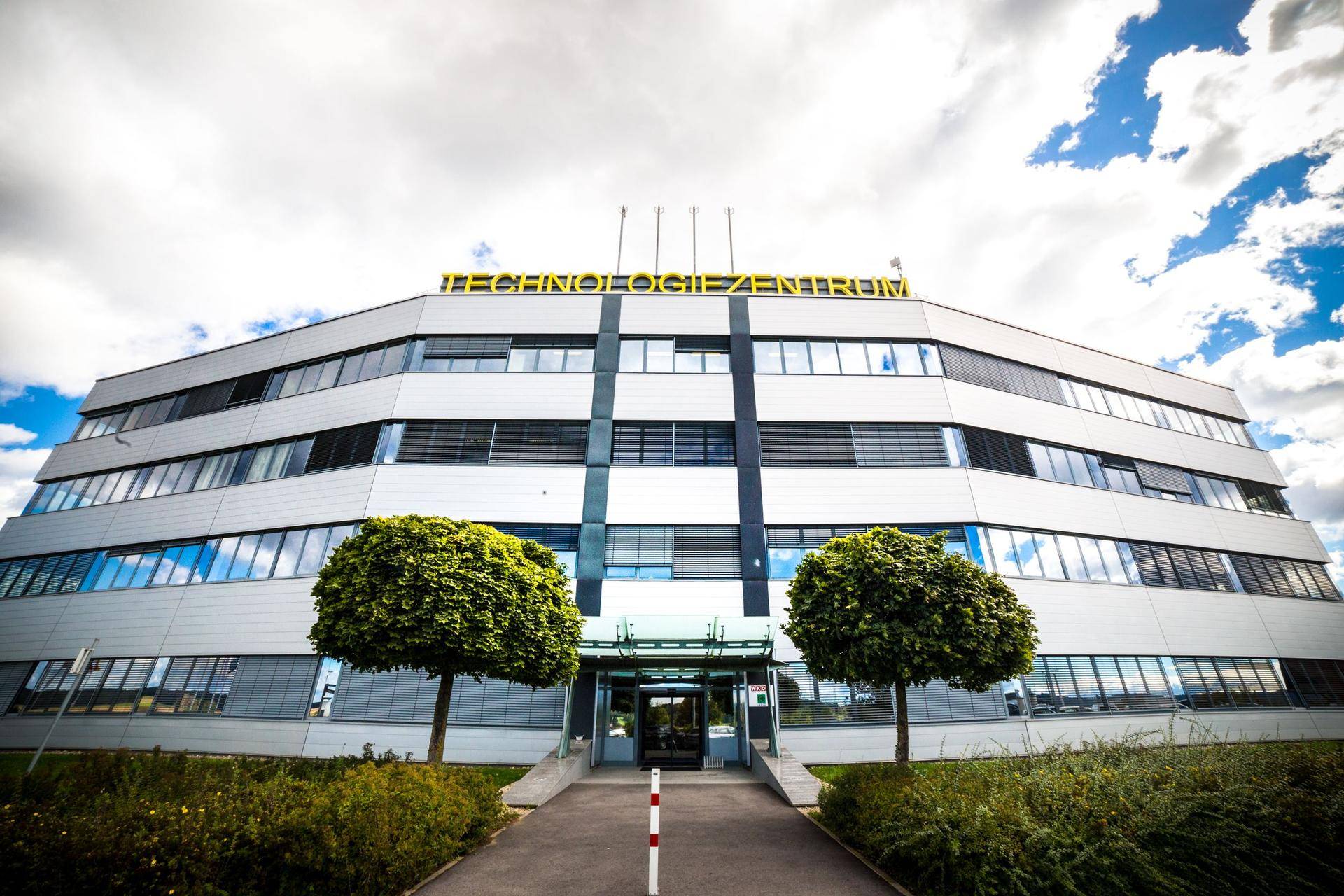 Modernes Bürogebäude mit vielen Fenstern und einem Technologiezentrum-Schriftzug unter bewölktem Himmel.